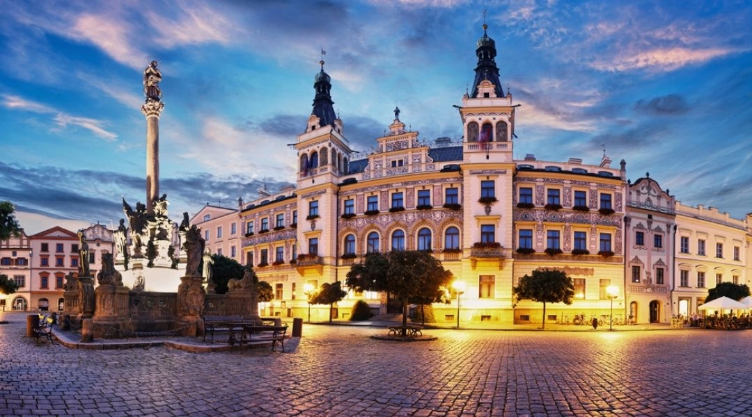 Historyczny rynek w Pardubicach z ozdobnymi kamienicami i kolumną na placu.