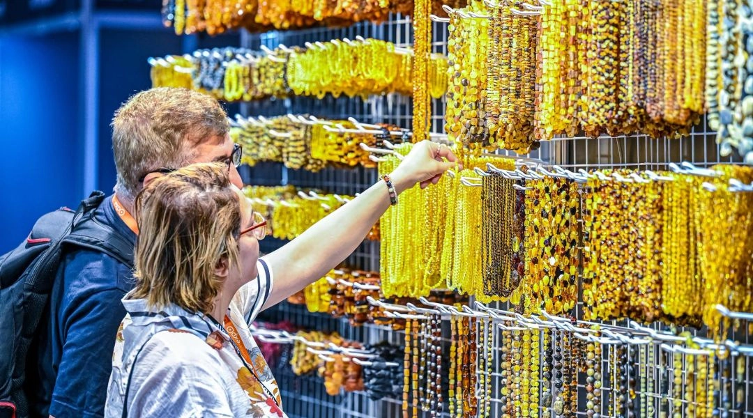 Kobieta ogląda naszyjniki i biżuterię z bursztynu prezentowaną na stoisku targowym.