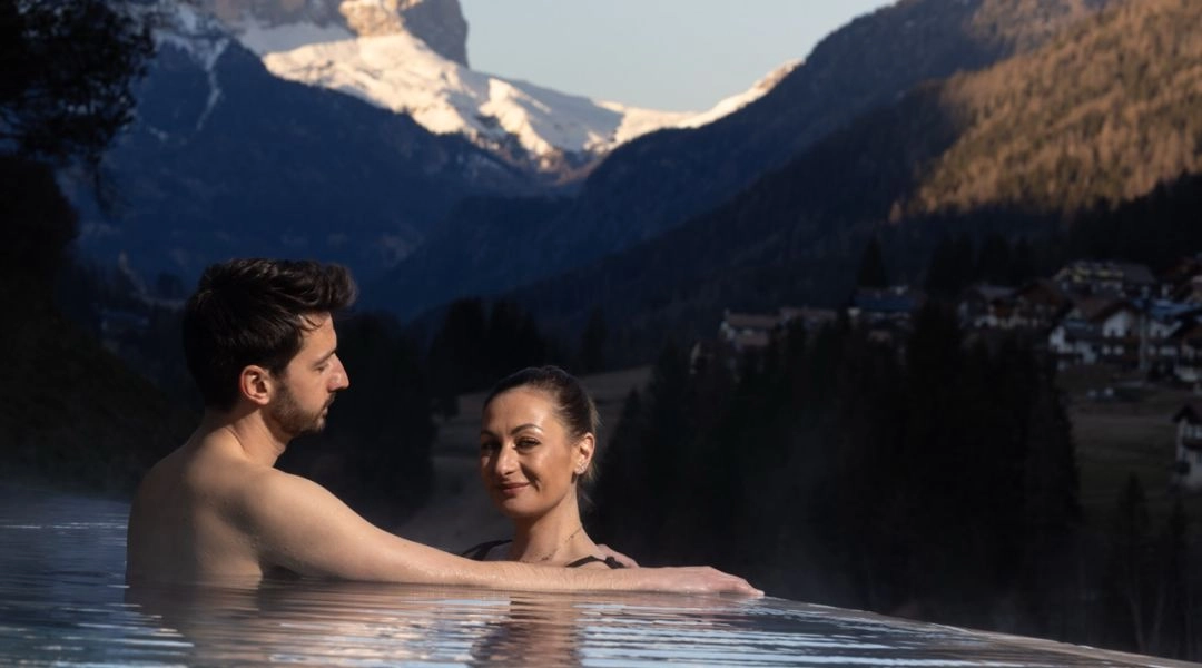 Para w basenie infinity z widokiem na Dolomity w Val di Fassa w Trentino.