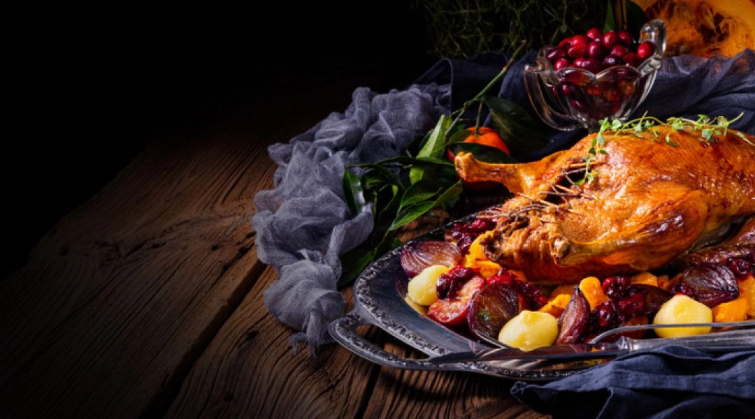 Pieczona gęś w całości podana na srebrnej tacy z warzywami, ziemniakami i żurawiną.