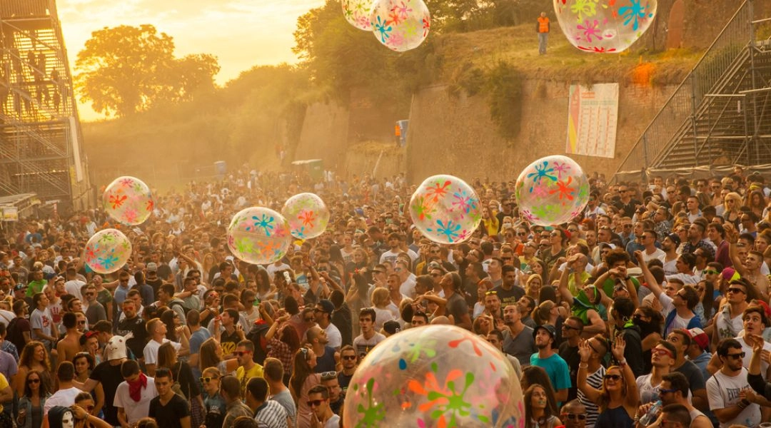 Tłum uczestników Sunrise Festival bawi się o zachodzie słońca wśród dużych przezroczystych piłek z kolorowymi wzorami.