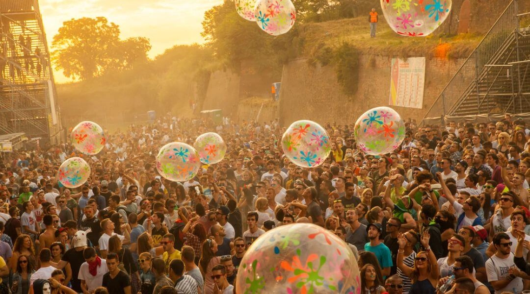 Tłum uczestników Sunrise Festival bawi się o zachodzie słońca wśród dużych przezroczystych piłek z kolorowymi wzorami.