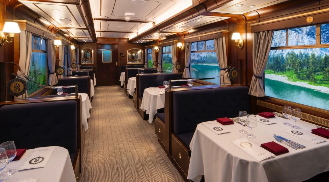 Wnętrze restauracji Royal Railway stylizowanej na elegancki wagon kolejowy z nakrytymi stolikami i ekranami w oknach.
