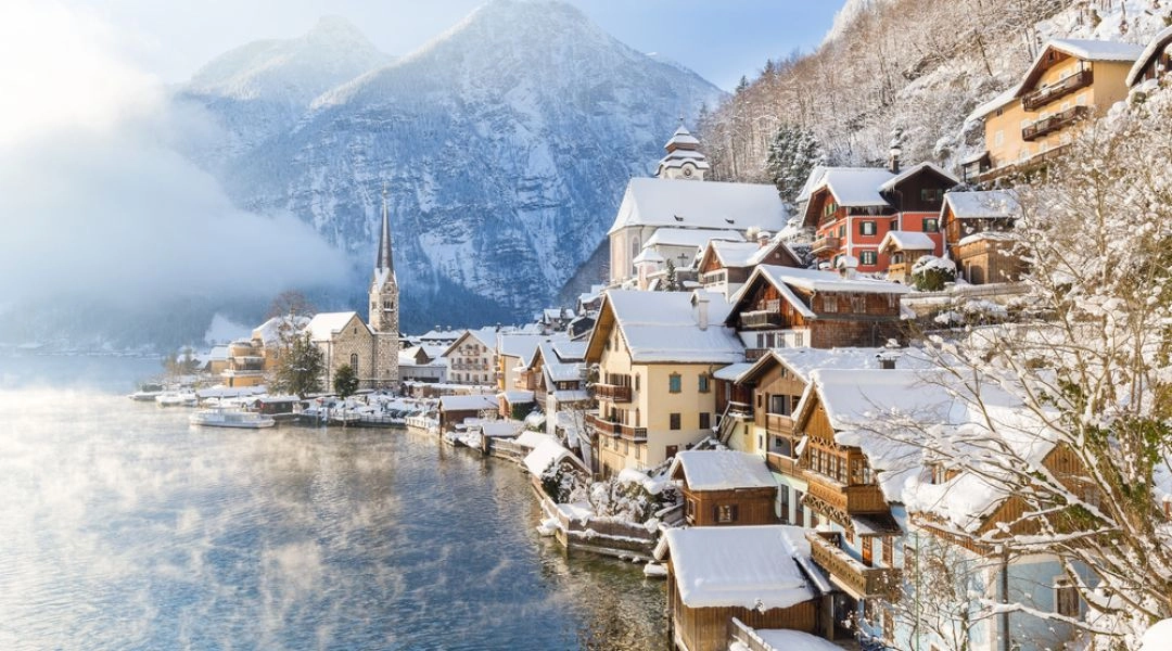 Hallstatt w grudniu, miasteczko nad jeziorem w Alpach z ośnieżoną zabudową i górskim tłem.