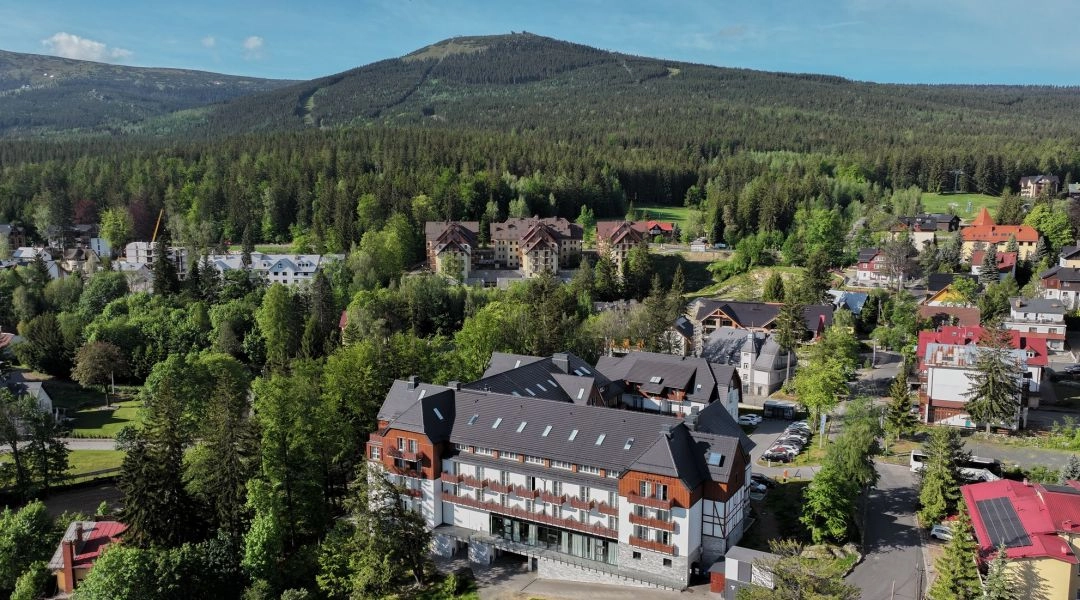 Panorama Szklarskiej Poręby z zabudowaniami otoczonymi lasem i zalesionymi zboczami Karkonoszy.