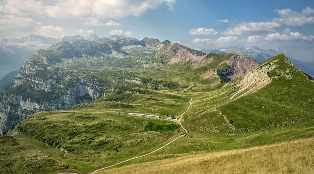 Szeroki górski krajobraz w Trentino z widoczną ścieżką prowadzącą przez zielone grzbiety i alpejskie hale.