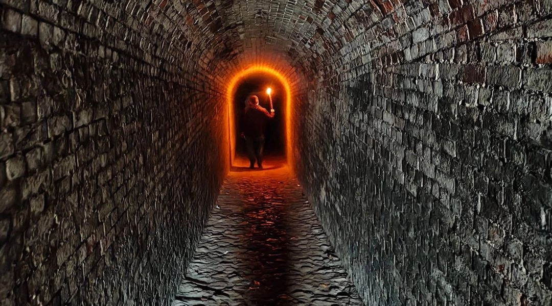 Ceglany tunel w Forcie Blizne i postać z pochodnią podczas Ścieżki Duchów w Warszawie