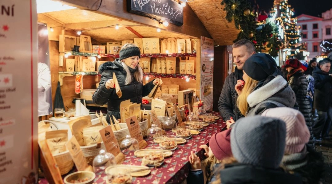 Odwiedzający jarmark stoją przy stoisku z lokalnymi przekąskami i ozdobami świątecznymi.