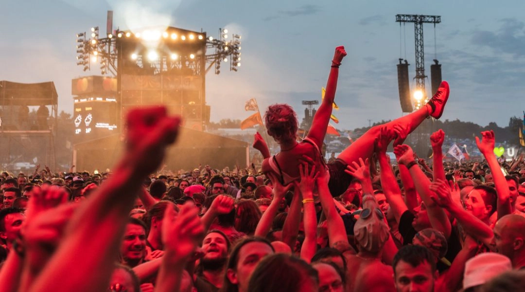 Publiczność podczas Pol’and’Rock Festival niesie uczestniczkę nad tłumem przed dużą plenerową sceną.
