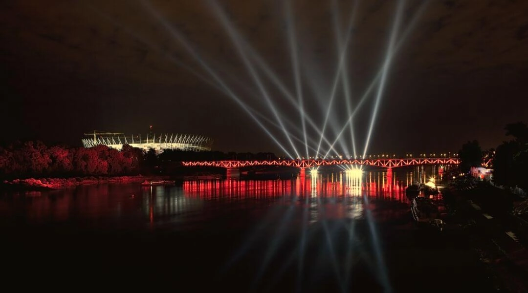 Laserowy pokaz świetlny nad Wisłą w Warszawie, widok na most i miasto nocą.
