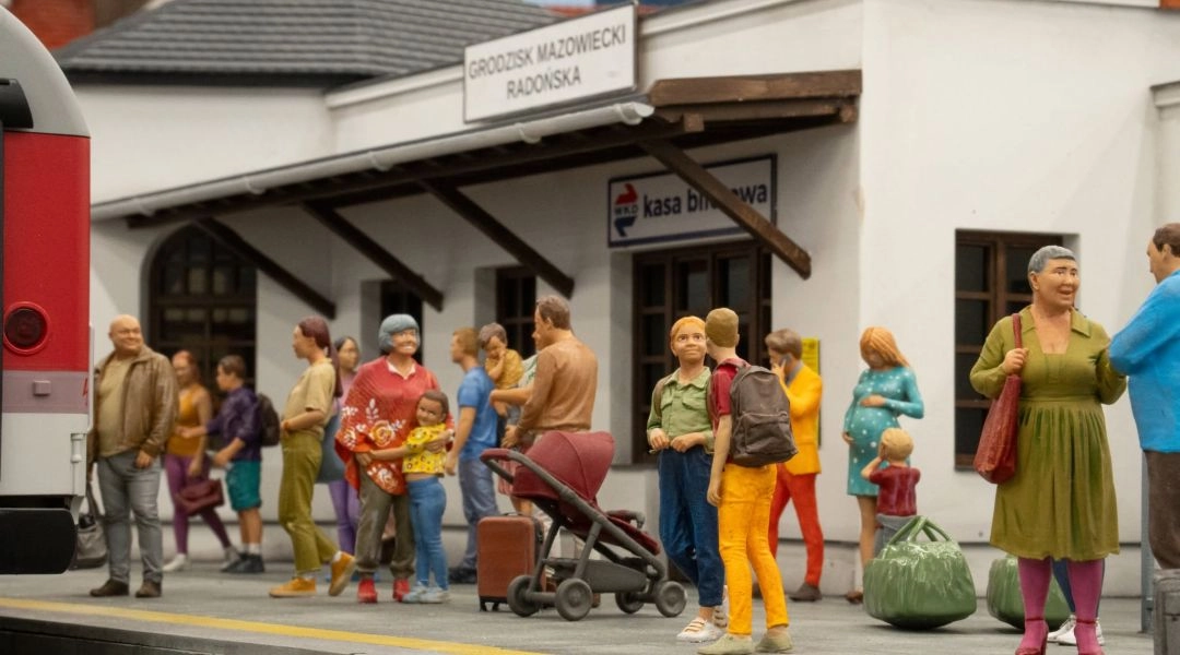 Miniaturowy peron stacji Grodzisk Mazowiecki Radońska z figurkami podróżnych i fragmentem pociągu na makiecie Kolejkowa.