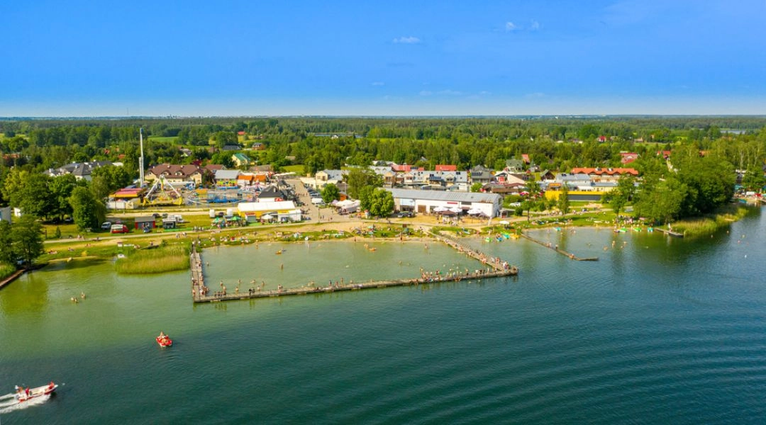 Jezioro Białe w Okunince z plażą, pomostami i turystyczną zabudową przy brzegu.