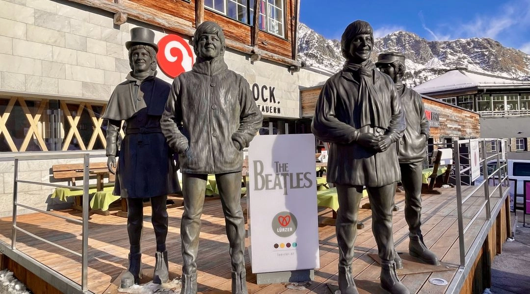 Rzeźby członków The Beatles w Obertauern na tle alpejskiej zabudowy i gór.