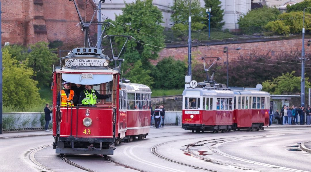 Zabytkowe czerwono-białe tramwaje jadą po torach podczas wydarzenia w Warszawie.