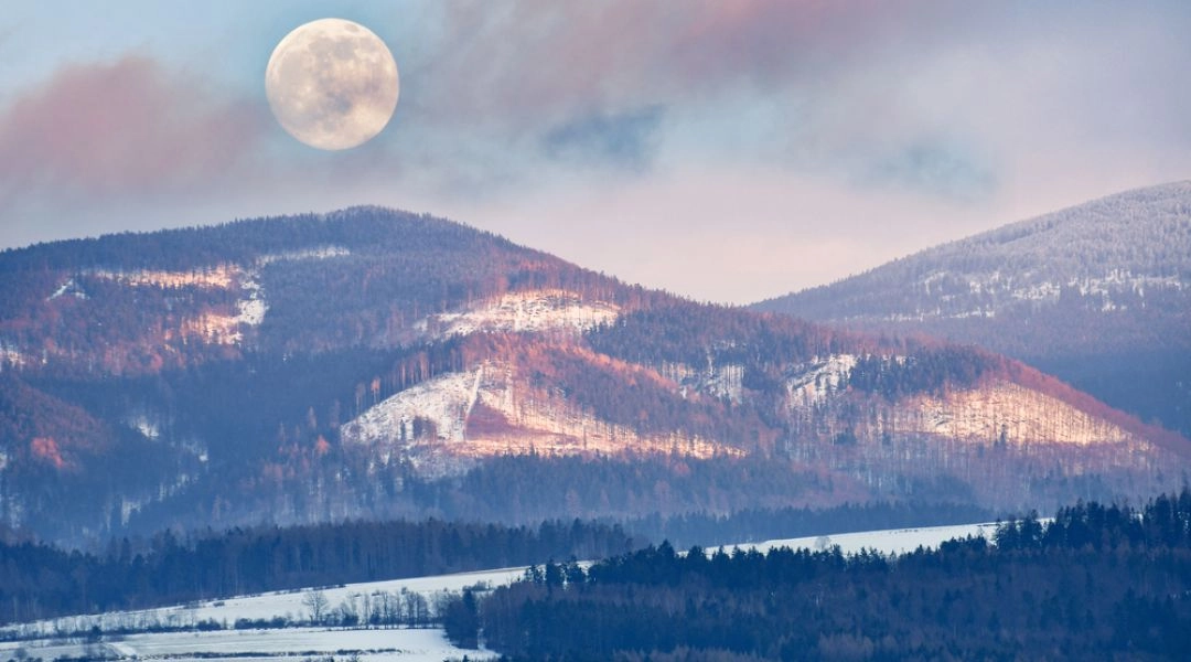 Zimowy krajobraz gór Dolnego Śląska o zmierzchu z widocznym księżycem.