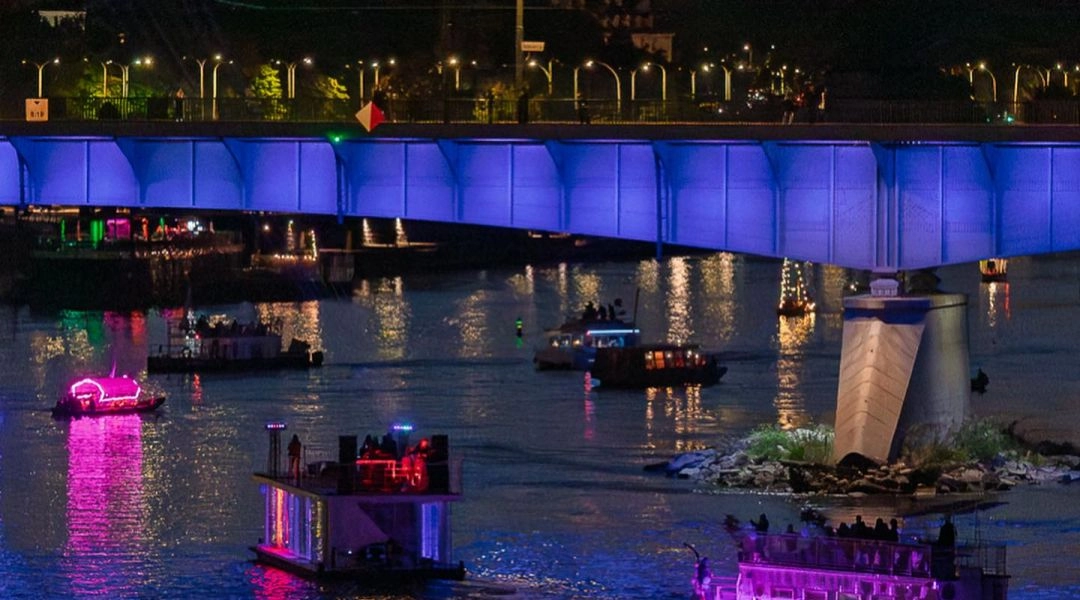 Rozświetlone łodzie płyną nocą po Wiśle pod podświetlonym mostem w Warszawie.