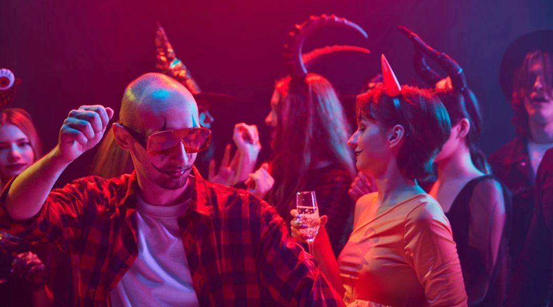 Tłum bawi się pod dyskotekową kulą podczas halloweenowej imprezy w klubie.