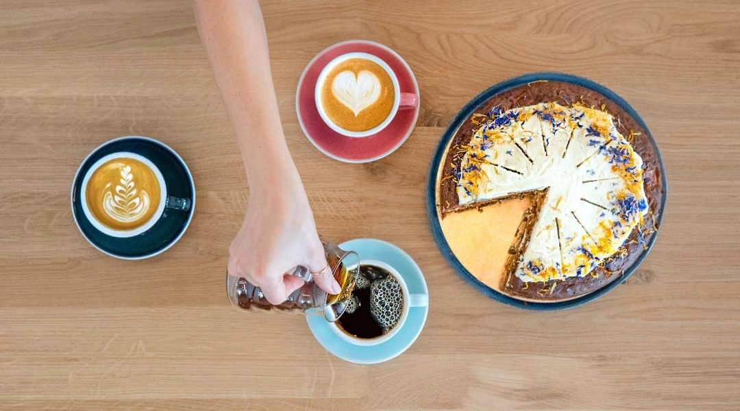 Filiżanki kawy i ciasto na drewnianym stole w warszawskiej kawiarni.