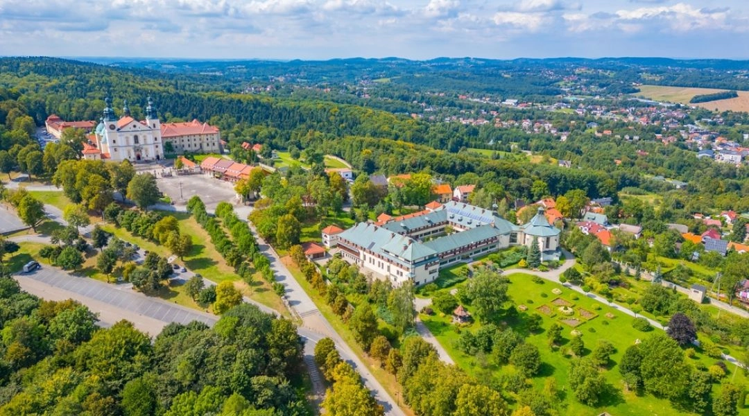 Widok z lotu ptaka na bazylikę i klasztor Bernardynów w Kalwarii Zebrzydowskiej, otoczone lasami i zielonymi wzgórzami.