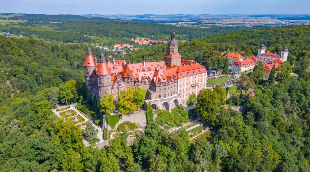 Zamek Książ widziany z lotu ptaka, otoczony gęstym lasem i tarasowymi ogrodami.