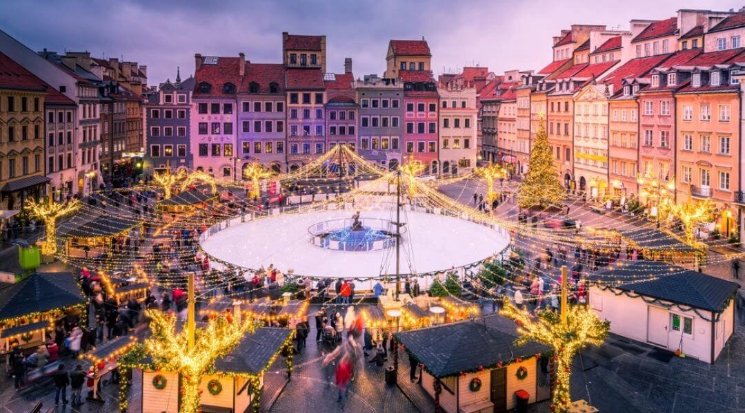 Widok z góry na Rynek Starego Miasta z lodowiskiem pośrodku oraz stoiskami jarmarku i choinkami w świątecznej iluminacji.