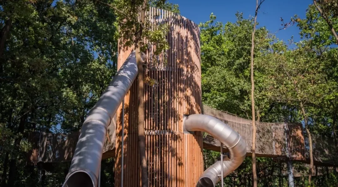 Plac zabaw w Parku Żerańskim, drewniana konstrukcja wśród drzew, zjeżdżalnie.