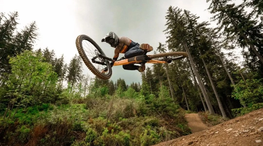 Rowerzysta wykonuje wysoki skok nad leśną trasą w Riders Park Donovaly.