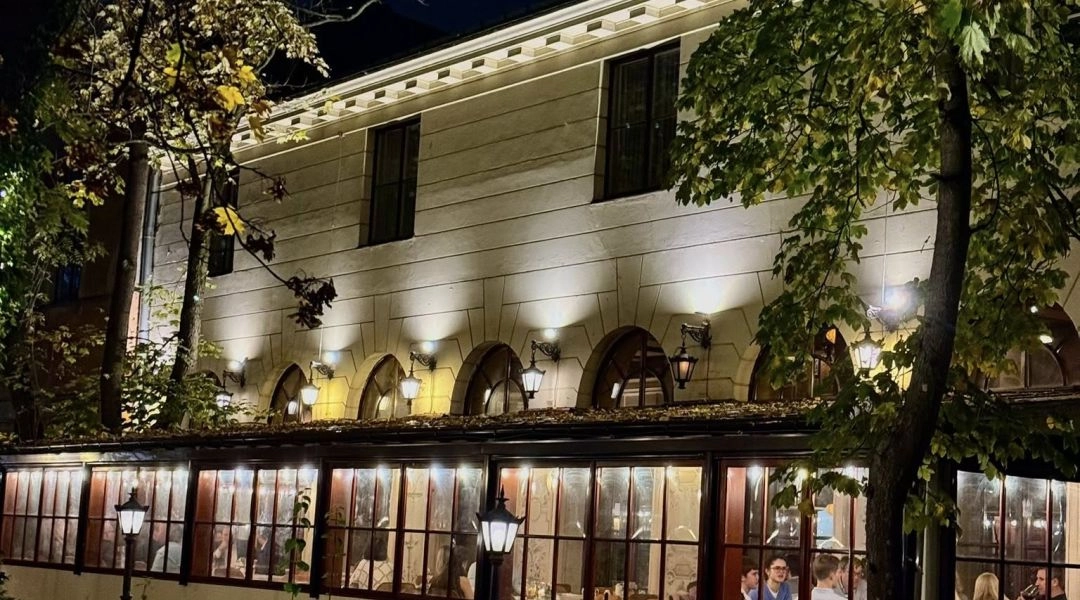 Budynek restauracji W Ogrodzie w Warszawie wieczorem, oświetlona oranżeria i drzewa wokół.