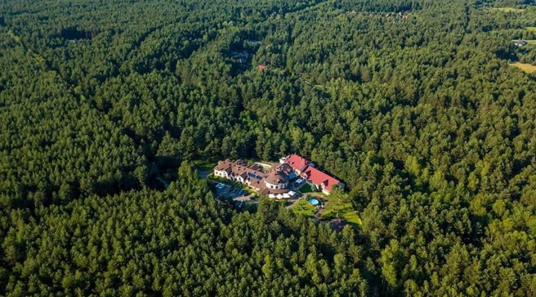 Hotel położony pośród rozległego, zielonego lasu widziany z lotu ptaka.