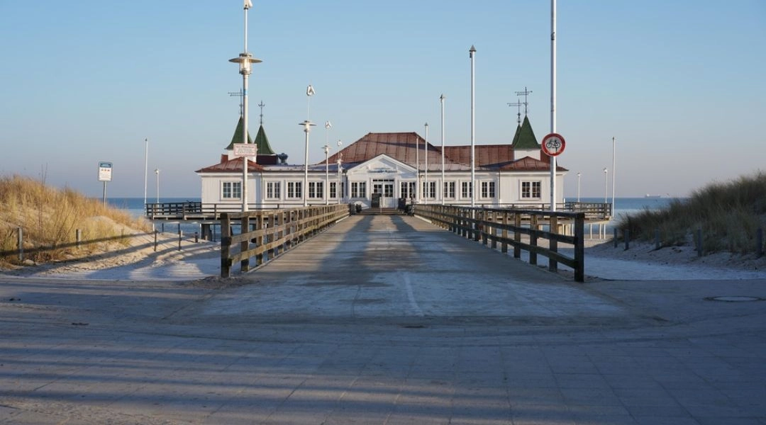 Zabytkowe molo w Ahlbecku na wyspie Uznam, prowadzące do białego budynku nad Bałtykiem.
