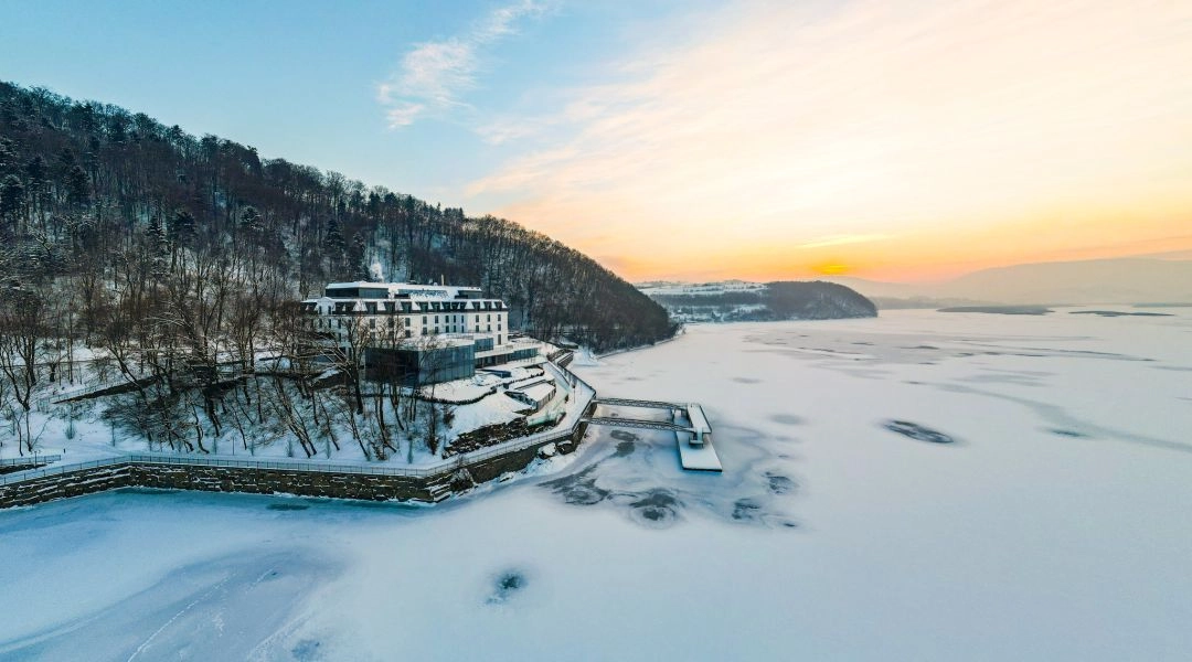 Heron Live Hotel położony nad zamarzniętym Jeziorem Rożnowskim, otoczony lasem, widok z lotu ptaka o wschodzie słońca.