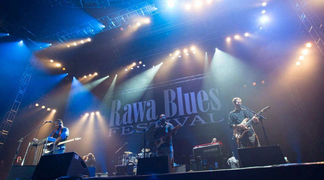 Zespół grający na scenie Rawa Blues Festival w niebieskim i żółtym świetle reflektorów.