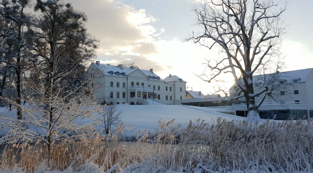 Hanza Pałac przykryty śniegiem, widoczna bryła pałacu i parkowe drzewa po zimowych opadach, delikatne światło popołudnia.