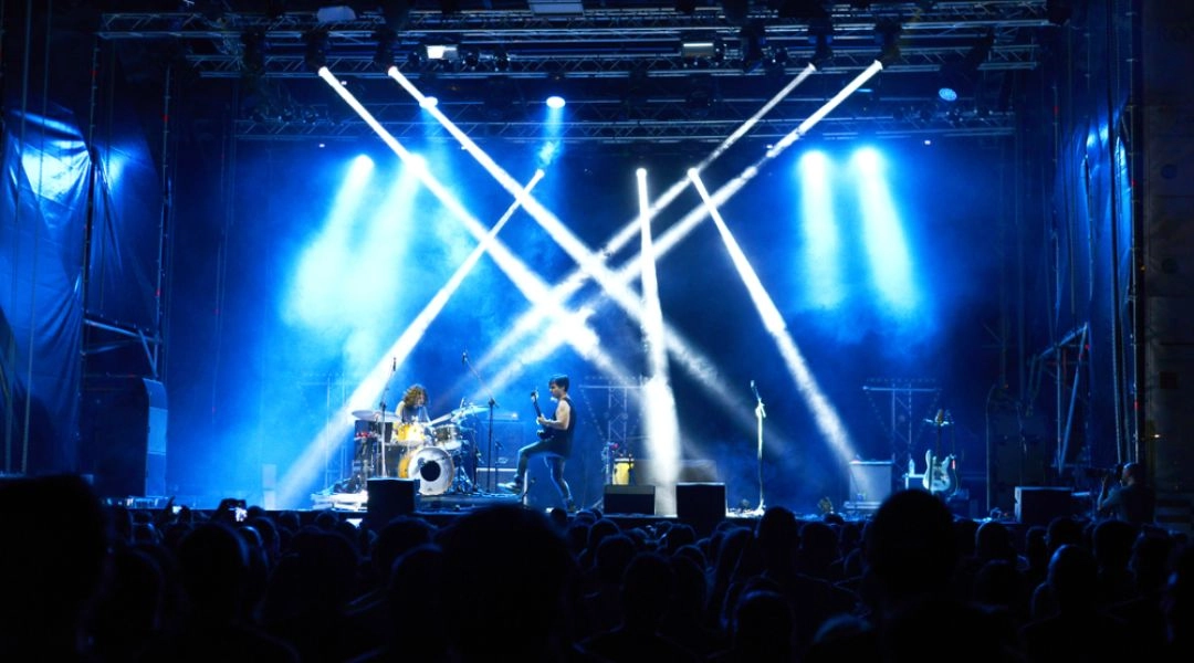 Plenerowy koncert w Warszawie, scena oświetlona reflektorami i publiczność przed zespołem