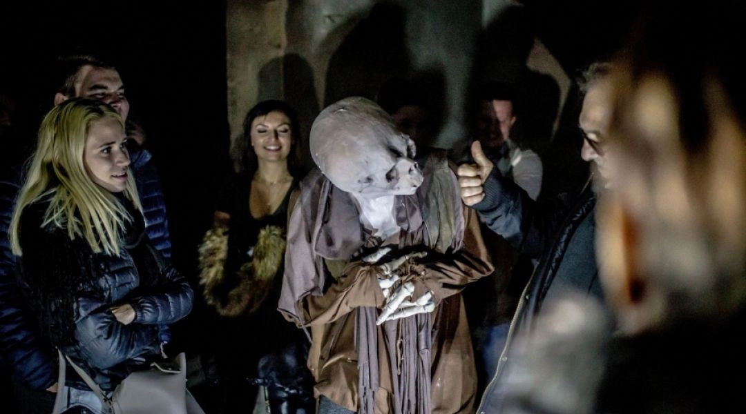 Aktor w charakteryzacji upiora pochyla się w stronę uczestników nocnego zwiedzania zamku Książ.