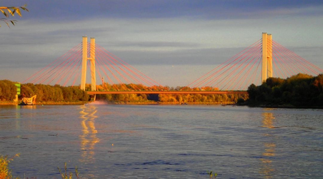 Most Siekierkowski nad Wisłą w Warszawie widziany z brzegu rzeki o zachodzie słońca.