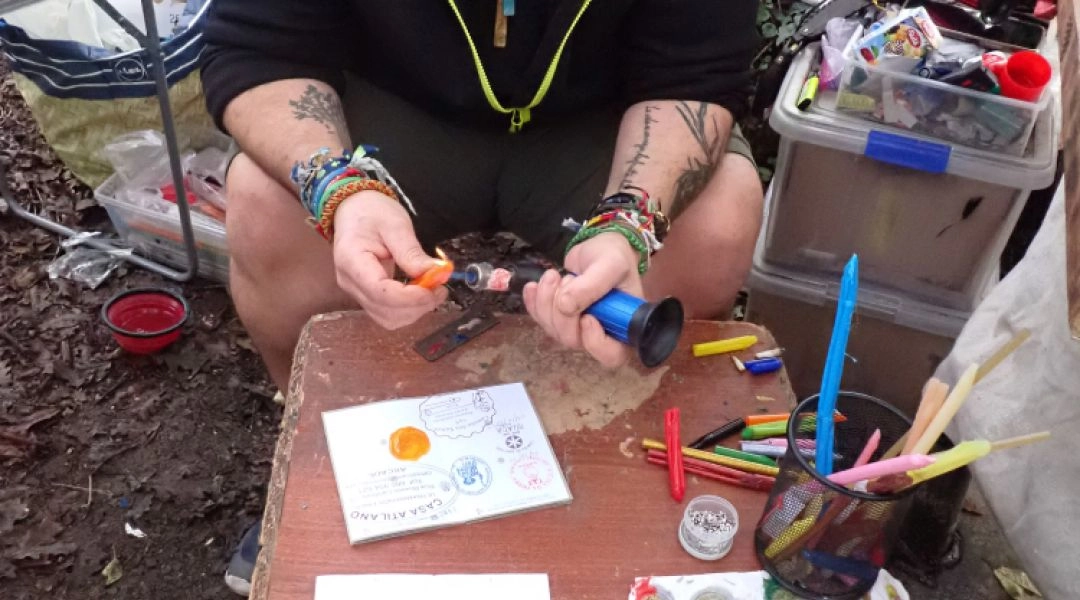 Pielgrzym siedzący przy drewnianym stoliku, wykonujący pieczątki do paszportu Camino, wokół farby i przybory.