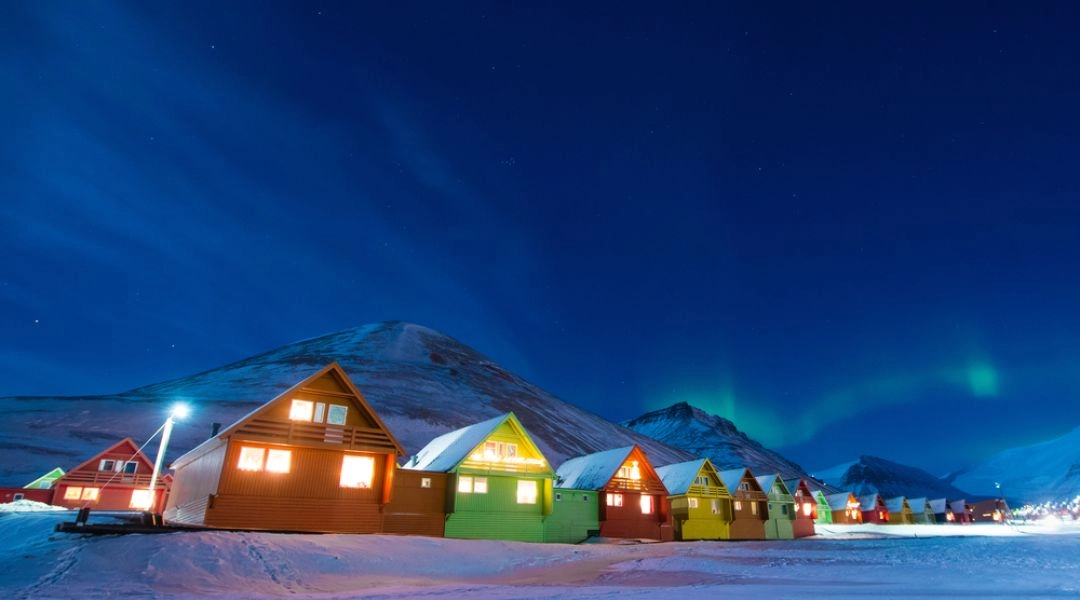 Kolorowe domy Longyearbyen zimą, śnieg, nocne niebo i zorza polarna nad Svalbardem.