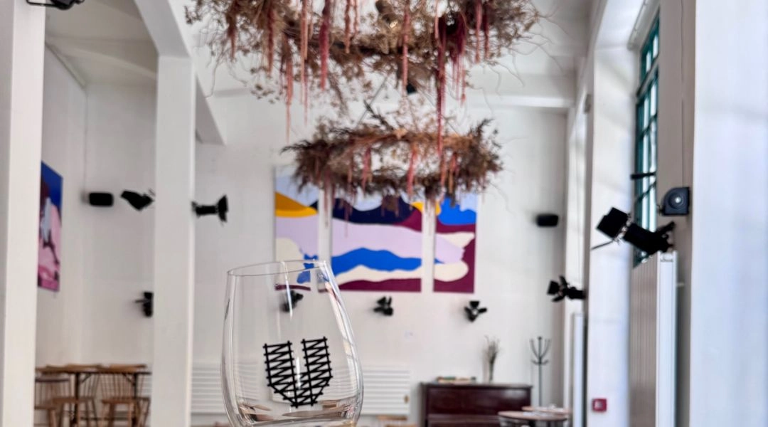 Kieliszek słowackiego wina w jasnym wnętrzu winiarni z drewnianymi stolikami, obrazami i dekoracją pod sufitem.