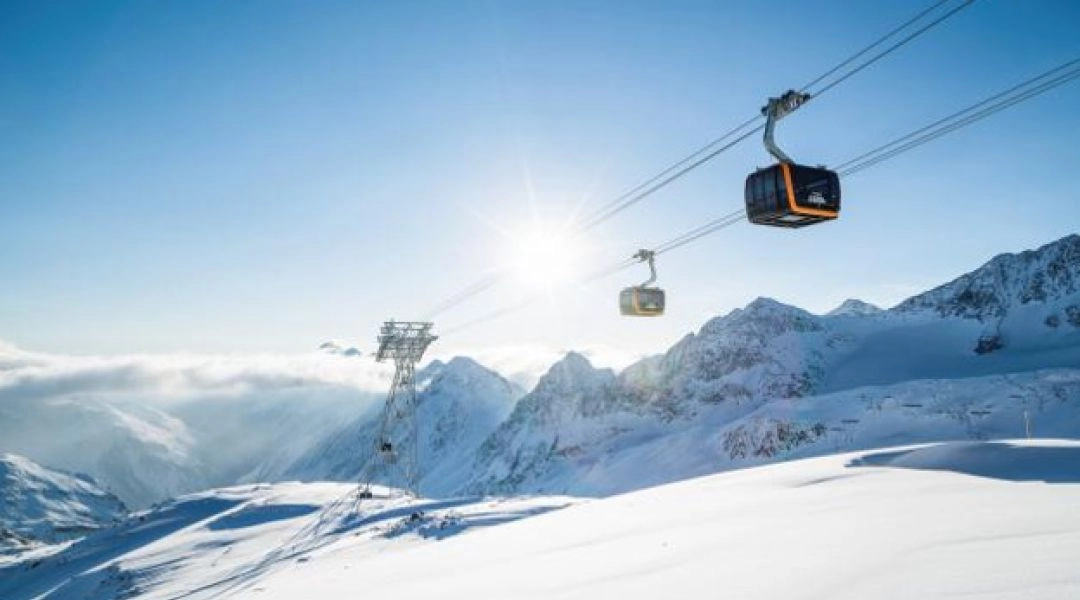 Gondole kolejki nad ośnieżonym zboczem lodowca Stubai, z górskimi szczytami w tle.