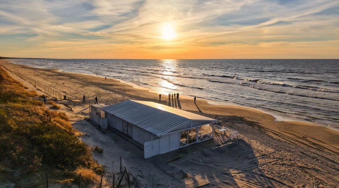 Pusta plaża w Krynicy Morskiej widziana z góry podczas zachodu słońca, z drewnianym kompleksem restauracyjnym na wydmie.