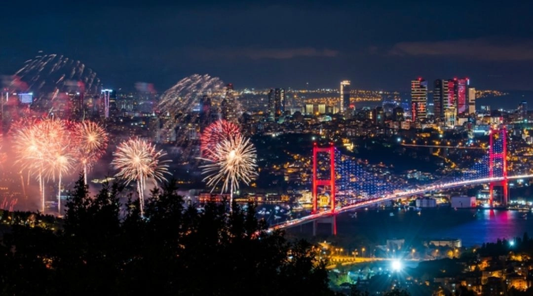 Panorama Stambułu nocą z fajerwerkami nad Bosforem i podświetlonym mostem.