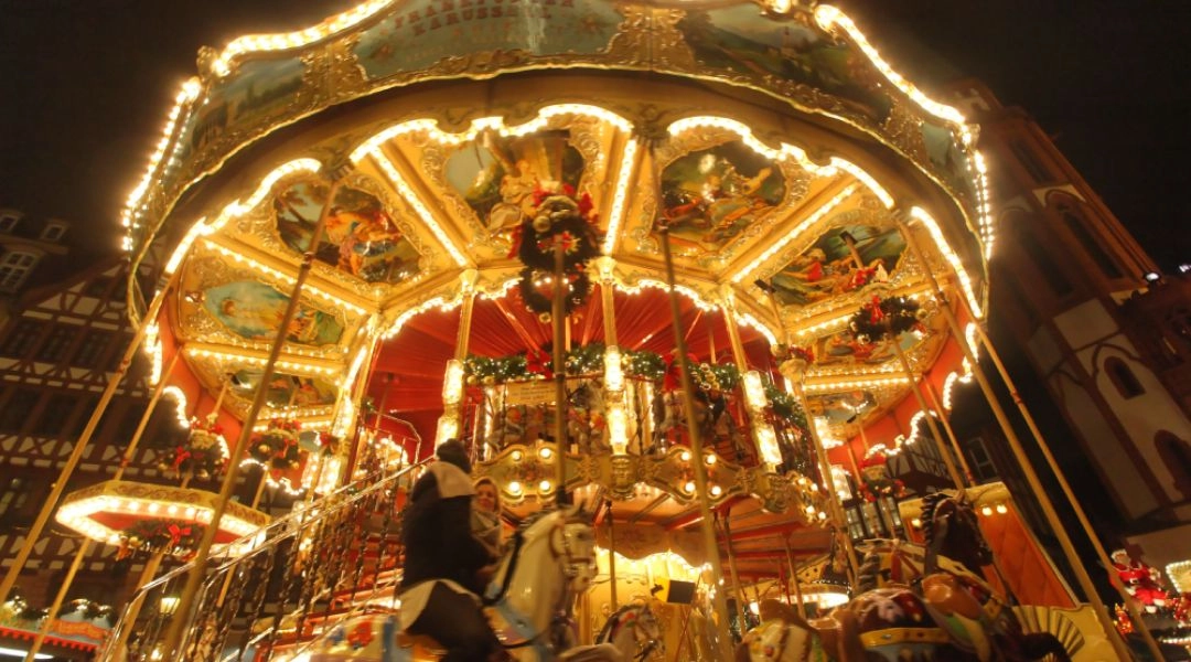 Oświetlona karuzela z końmi na jarmarku świątecznym we Frankfurcie nad Menem, pełna dekoracji i świątecznych lamp.