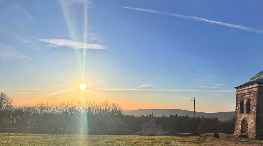Wschód słońca oglądany spod murów klasztoru na Świętym Krzyżu, z krzyżem i panoramą Gór Świętokrzyskich.