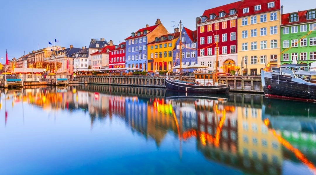 Kolorowe kamienice i drewniane łodzie odbijające się w wodzie kanału Nyhavn w Kopenhadze o zmierzchu.