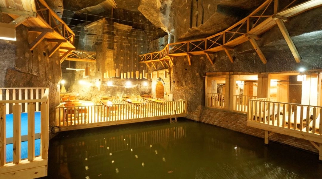 Podziemna komora Kopalni Soli Wieliczka z jeziorem solankowym, drewnianymi pomostami i oświetlonymi skalnymi ścianami.