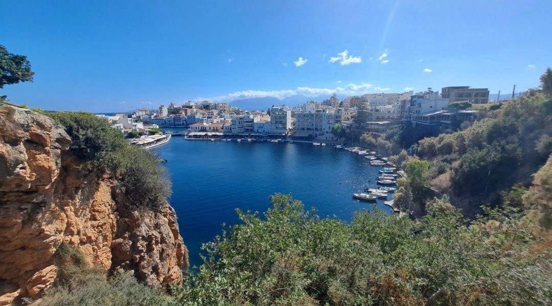 Widok na jezioro Voulismeni w Agios Nikolaos na Krecie, otoczone skałami, zielenią i białą zabudową miasta.