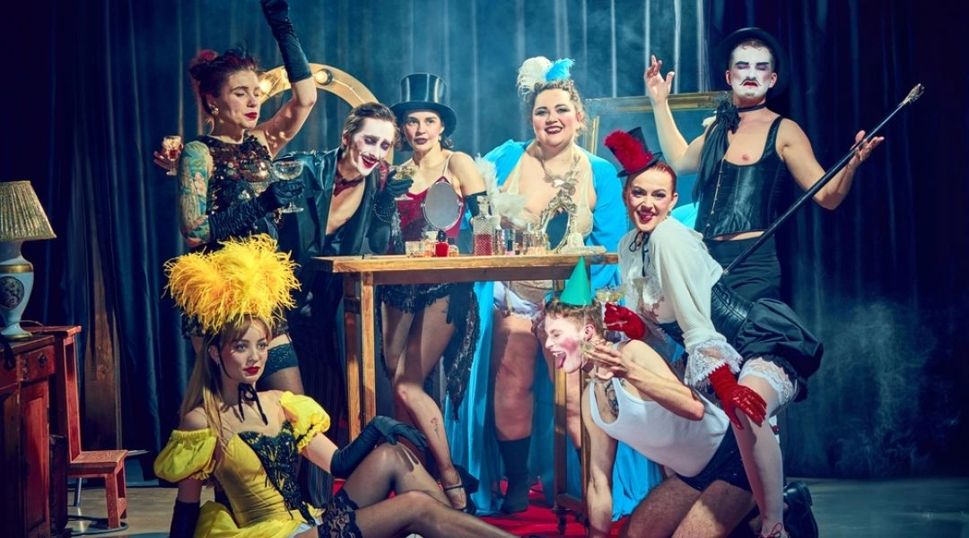Grupa artystek i artystów burleski w teatralnych kostiumach i makijażach podczas widowiska na scenie.