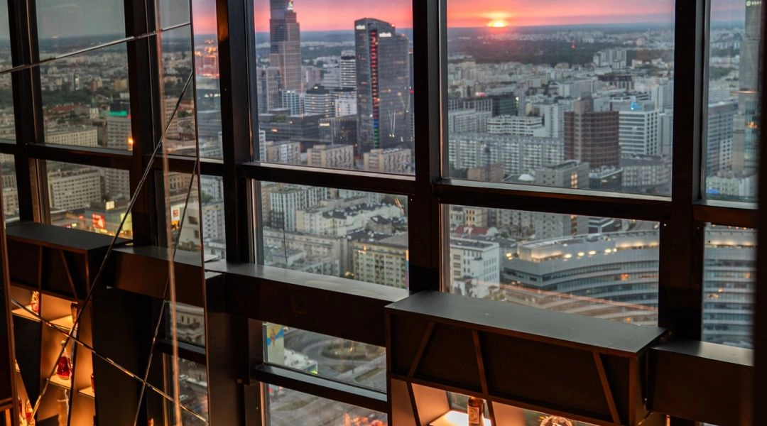 Widok z Panorama Sky Bar w Warszawie na centrum miasta i zachód słońca za oknami baru.