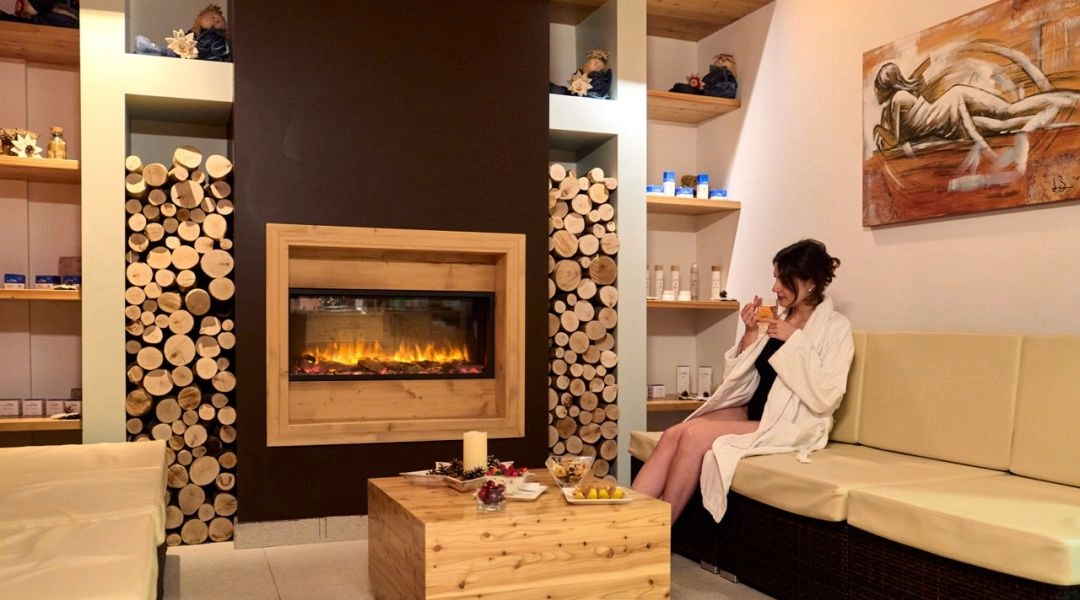 Strefa relaksu z kominkiem w hotelu wellness w Trentino, kobieta w szlafroku pije herbatę.